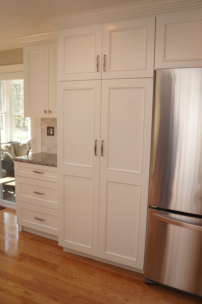 This is an example of a large transitional l-shaped kitchen pantry in Boston with recessed-panel cabinets, white cabinets, granite benchtops, subway tile splashback, stainless steel appliances, medium hardwood floors, with island and multi-coloured splashback.