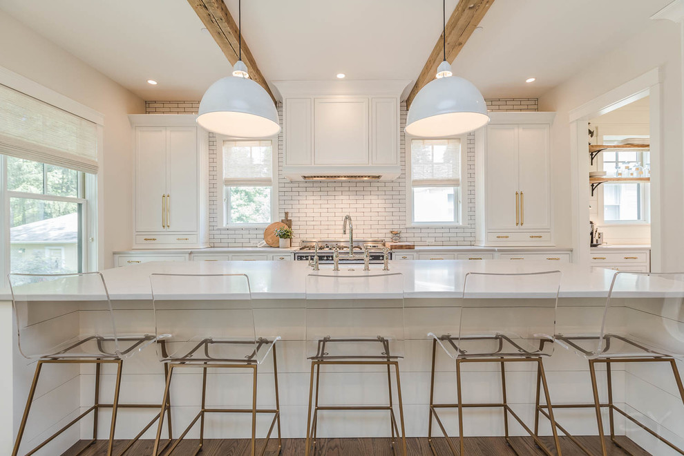 Photo of a mid-sized traditional l-shaped eat-in kitchen in Chicago with shaker cabinets, white cabinets, stainless steel appliances, with island, white splashback, subway tile splashback, dark hardwood floors, a farmhouse sink, solid surface benchtops and brown floor.