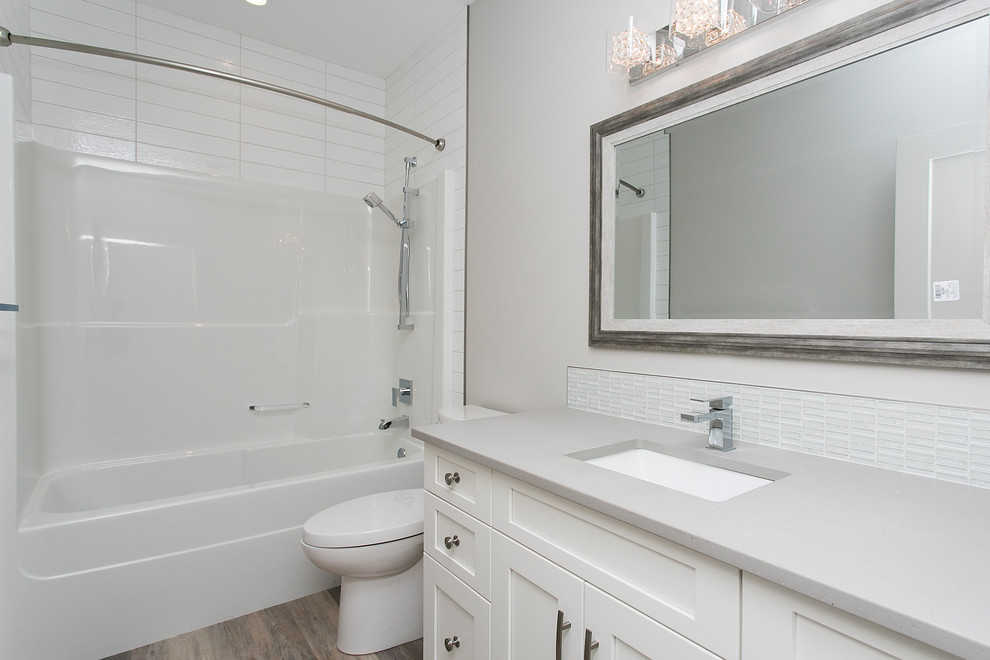This is an example of a mid-sized contemporary bathroom in Calgary with shaker cabinets, an alcove tub, a shower/bathtub combo, a one-piece toilet, glass tile, medium hardwood floors, an undermount sink and solid surface benchtops.