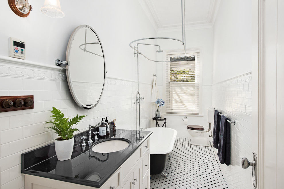 This is an example of a traditional bathroom in Melbourne with recessed-panel cabinets, white cabinets, a claw-foot tub, a shower/bathtub combo, a two-piece toilet, black and white tile, white tile, subway tile, white walls, an undermount sink, a shower curtain and black benchtops.