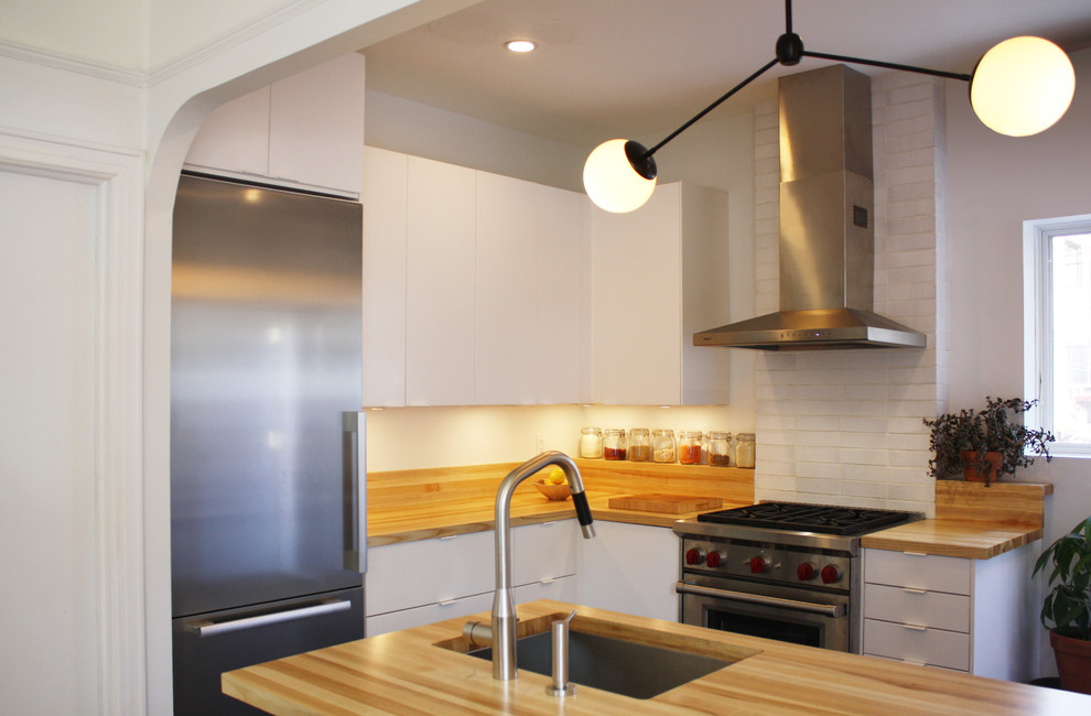 Photo of a mid-sized modern l-shaped eat-in kitchen in New York with an undermount sink, flat-panel cabinets, white cabinets, wood benchtops, stainless steel appliances, vinyl floors and with island.