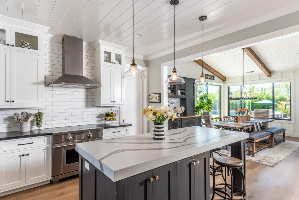 Photo of a large country u-shaped eat-in kitchen in San Francisco with a farmhouse sink, shaker cabinets, white cabinets, white splashback, subway tile splashback, panelled appliances, medium hardwood floors, with island, brown floor, white benchtop, timber and quartz benchtops.