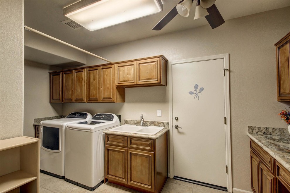 Inspiration for a mid-sized traditional galley utility room in Phoenix with a double-bowl sink, raised-panel cabinets, medium wood cabinets, granite benchtops, beige walls, ceramic floors and a side-by-side washer and dryer.