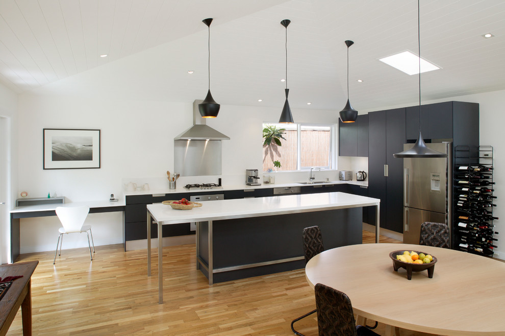 Mid-sized midcentury l-shaped open plan kitchen in Sydney with black cabinets, quartz benchtops, stainless steel appliances, a double-bowl sink, recessed-panel cabinets, white splashback, ceramic splashback, light hardwood floors and with island.