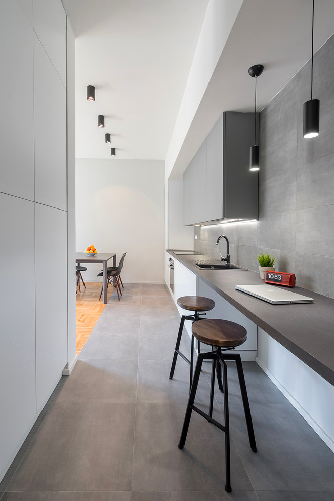 This is an example of a modern galley kitchen in Florence with flat-panel cabinets, grey cabinets, grey splashback, porcelain floors, grey floor, a drop-in sink, black appliances, no island and black benchtop.