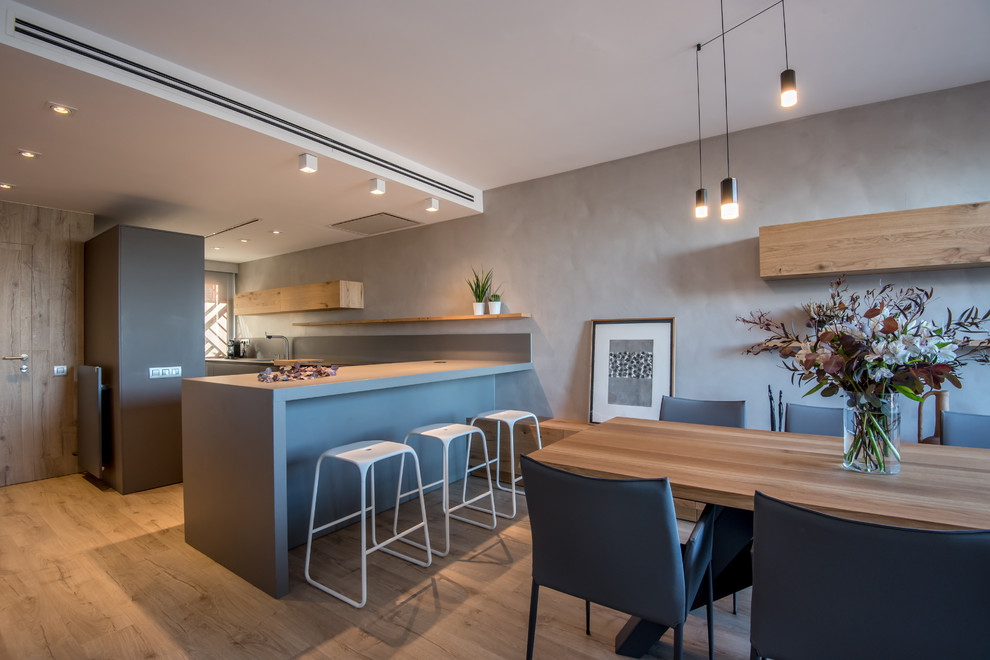 This is an example of a large contemporary open plan dining in Barcelona with grey walls, laminate floors, a two-sided fireplace, a metal fireplace surround and brown floor.