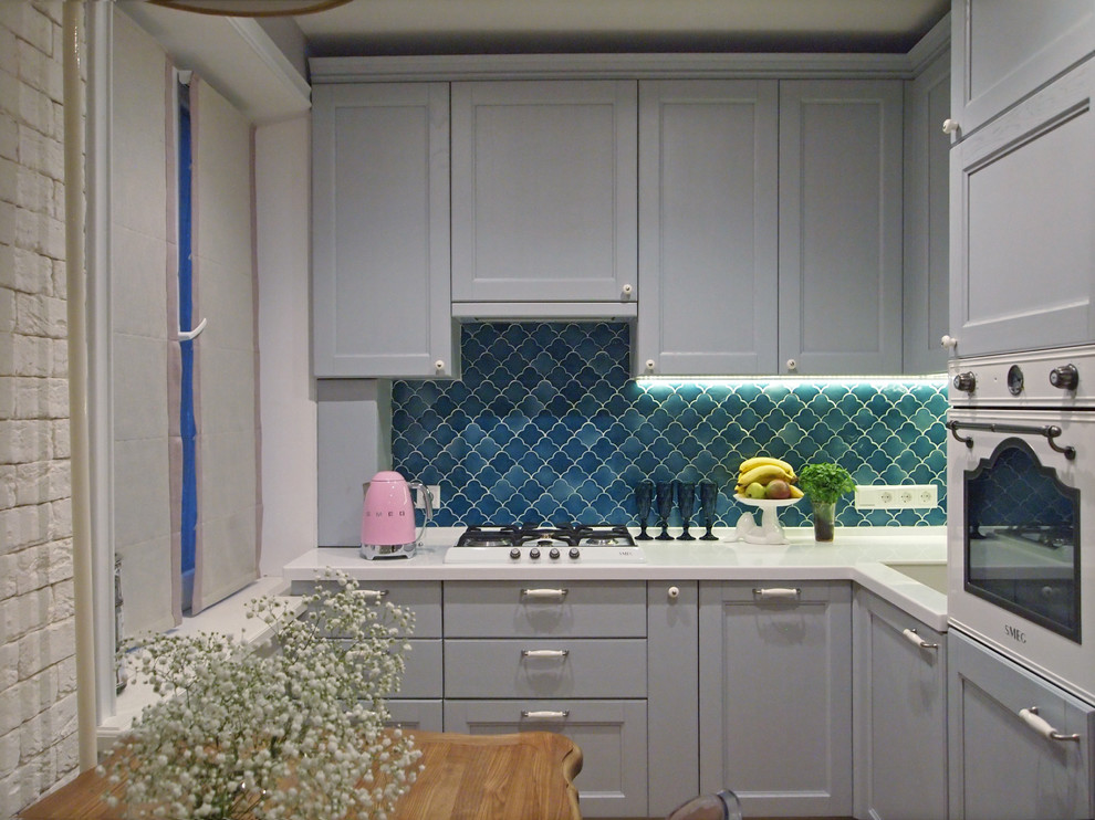 This is an example of a small scandinavian l-shaped eat-in kitchen in Moscow with a single-bowl sink, recessed-panel cabinets, grey cabinets, solid surface benchtops, blue splashback, ceramic splashback, white appliances, laminate floors, no island and beige floor.