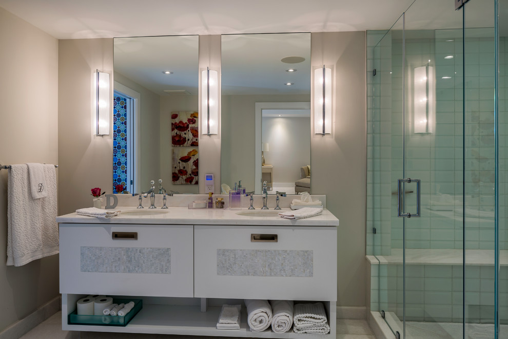 This is an example of a large contemporary 3/4 bathroom in Miami with glass-front cabinets, white cabinets, a corner tub, an open shower, a one-piece toilet, white tile, stone slab, white walls, ceramic floors, a drop-in sink and solid surface benchtops.