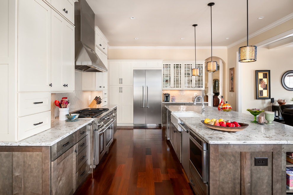 This is an example of a mid-sized transitional l-shaped eat-in kitchen in Atlanta with a farmhouse sink, shaker cabinets, white cabinets, granite benchtops, white splashback, subway tile splashback, stainless steel appliances, medium hardwood floors, multiple islands and brown floor.