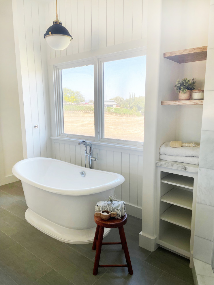 This is an example of a large country master bathroom in Santa Barbara with raised-panel cabinets, medium wood cabinets, a freestanding tub, a corner shower, white tile, marble, white walls, porcelain floors, an undermount sink, marble benchtops, grey floor, an open shower, white benchtops, an enclosed toilet, a double vanity, a built-in vanity and decorative wall panelling.