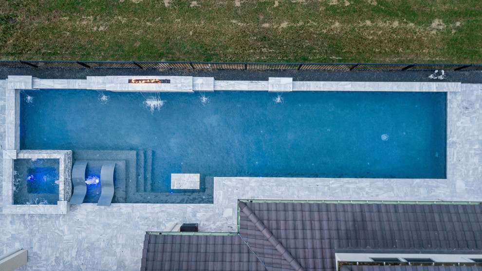 Bild på en stor funkis rektangulär pool på baksidan av huset, med naturstensplattor