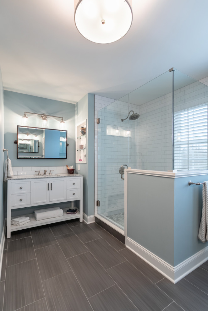Photo of a large transitional master bathroom in Burlington with shaker cabinets, white cabinets, a corner shower, a one-piece toilet, white tile, ceramic tile, blue walls, ceramic floors, an undermount sink, granite benchtops, grey floor, a hinged shower door, grey benchtops, a niche, a single vanity and a freestanding vanity.