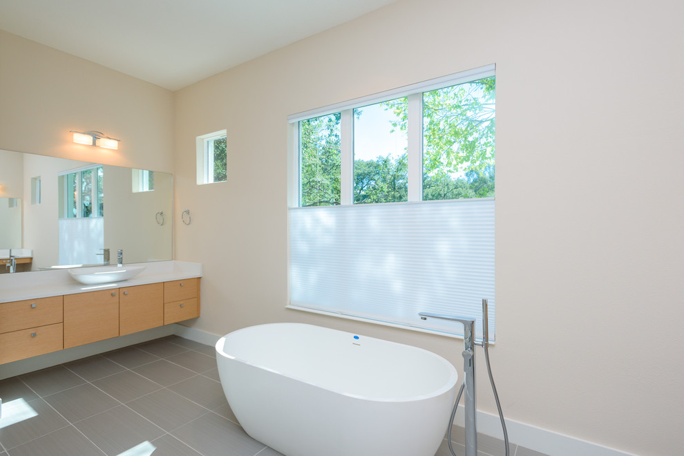 This is an example of a modern master bathroom in Tampa with flat-panel cabinets, light wood cabinets, a freestanding tub, gray tile, ceramic tile, ceramic floors, a vessel sink, engineered quartz benchtops, grey floor and beige walls.