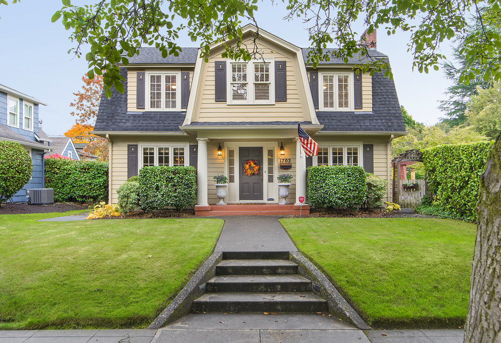 Photo of a traditional two-storey yellow house exterior in Portland with a gambrel roof and a shingle roof.