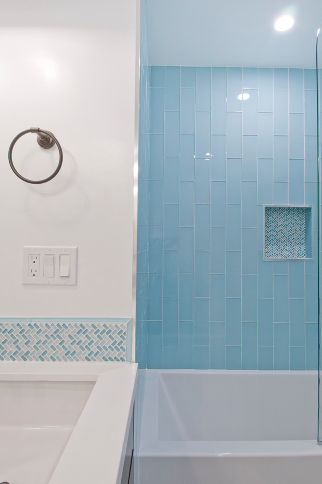 Photo of a large contemporary kids bathroom in Los Angeles with flat-panel cabinets, brown cabinets, an alcove tub, a shower/bathtub combo, blue tile, glass tile, white walls, porcelain floors, an undermount sink, solid surface benchtops, white floor and white benchtops.