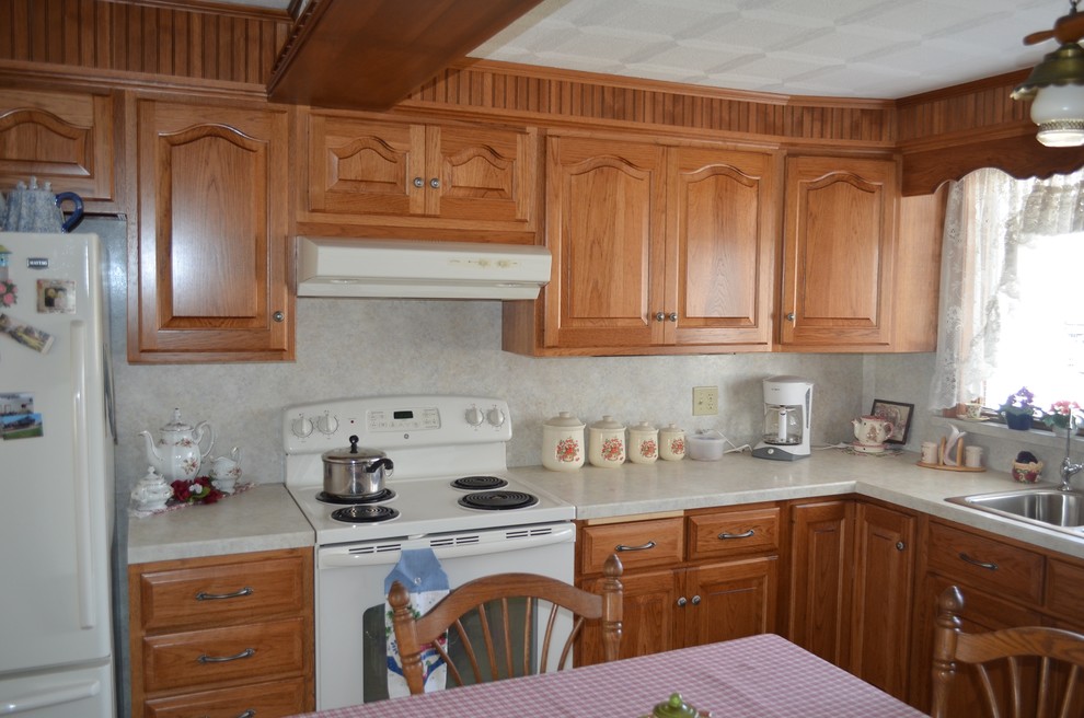 Example of a mid-sized classic l-shaped eat-in kitchen design with a drop-in sink, raised-panel cabinets, medium tone wood cabinets, laminate countertops, white backsplash and white appliances