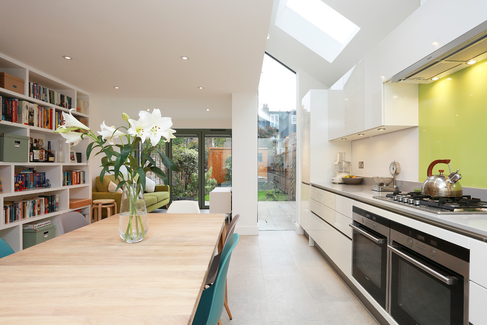 Large contemporary open plan kitchen in London with a drop-in sink, flat-panel cabinets, white cabinets, solid surface benchtops, yellow splashback, glass sheet splashback, stainless steel appliances, no island and beige floor.