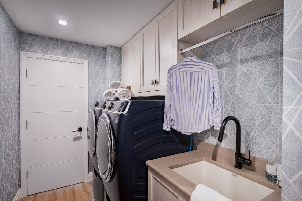 Design ideas for a transitional dedicated laundry room in Miami with a drop-in sink, flat-panel cabinets, white cabinets, blue walls, a side-by-side washer and dryer, beige benchtop and wallpaper.