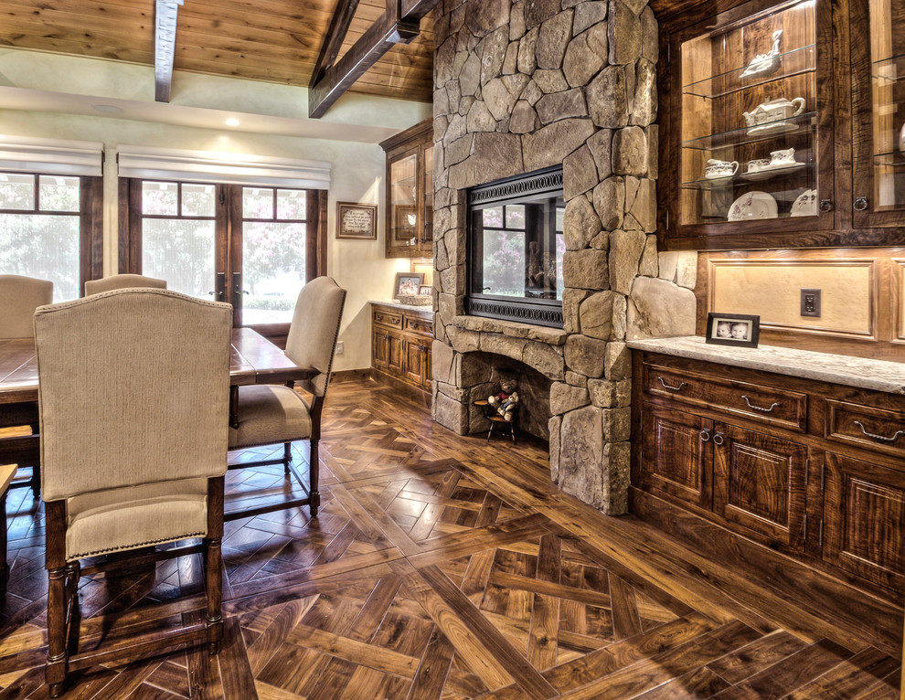 Example of a large mountain style medium tone wood floor kitchen/dining room combo design with white walls, a standard fireplace and a stone fireplace