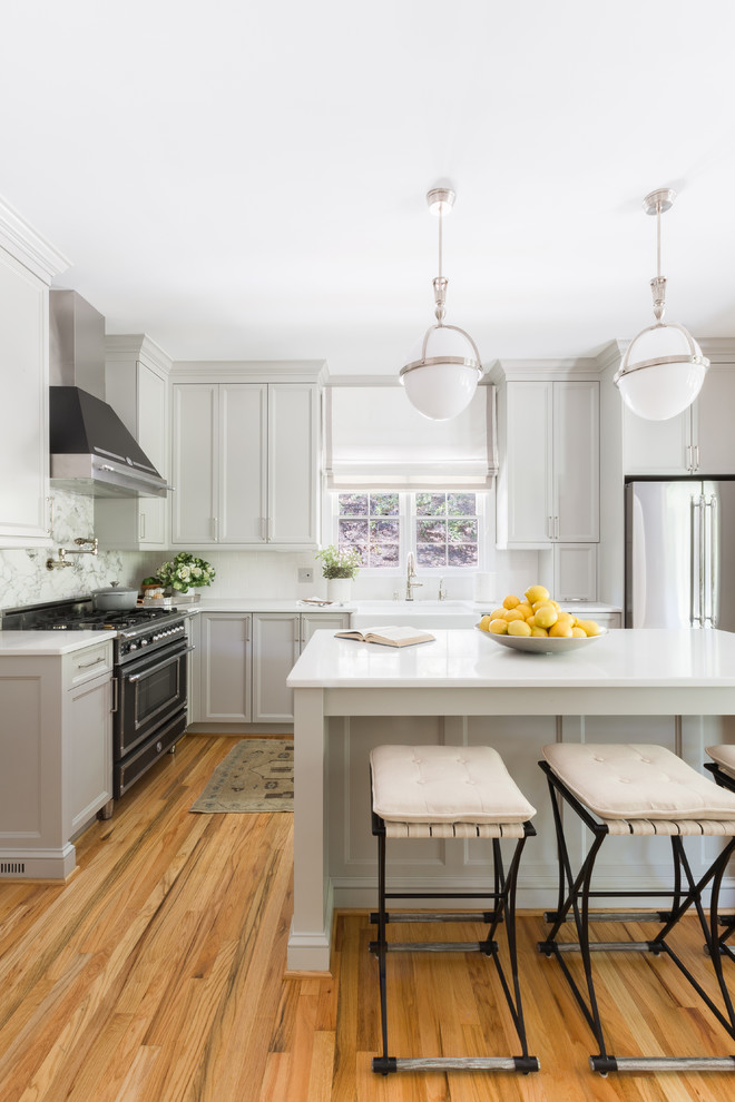 Inspiration for a transitional l-shaped kitchen in Other with a farmhouse sink, recessed-panel cabinets, grey cabinets, stainless steel appliances, medium hardwood floors, with island, brown floor and white benchtop.