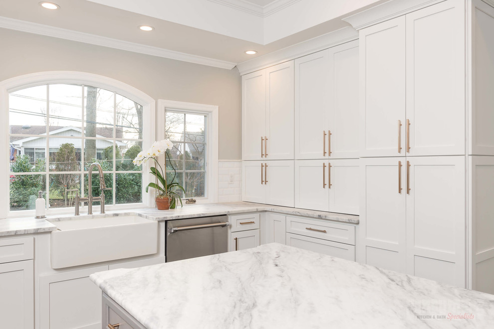Example of a large u-shaped plywood floor eat-in kitchen design in New York with a farmhouse sink, recessed-panel cabinets, white cabinets, quartzite countertops, white backsplash, ceramic backsplash, stainless steel appliances and an island