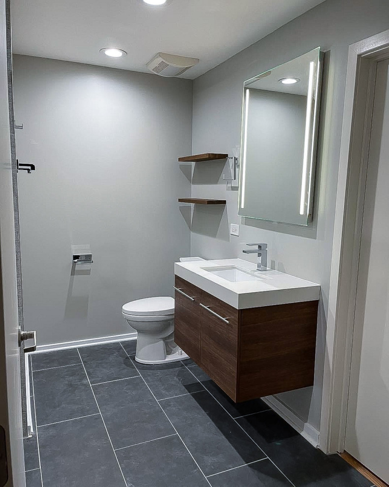 This is an example of a mid-sized modern bathroom in Chicago with flat-panel cabinets, brown cabinets, a drop-in tub, an alcove shower, a two-piece toilet, gray tile, porcelain tile, grey walls, porcelain floors, an undermount sink, engineered quartz benchtops, grey floor, a shower curtain, white benchtops, a niche, a single vanity and a floating vanity.