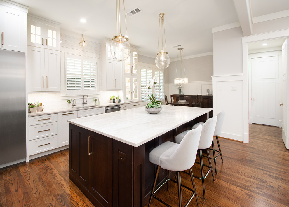 Design ideas for a large transitional l-shaped open plan kitchen in Dallas with a drop-in sink, flat-panel cabinets, white cabinets, quartzite benchtops, white splashback, ceramic splashback, stainless steel appliances, dark hardwood floors, with island, brown floor and grey benchtop.