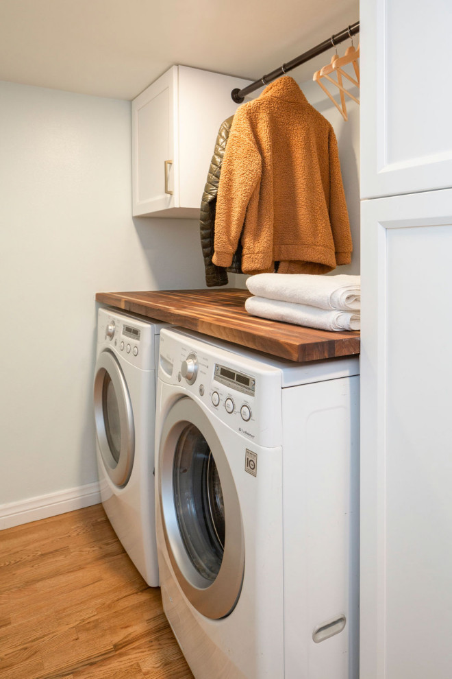 Small eclectic l-shaped utility room in Denver with shaker cabinets, white cabinets, wood benchtops, white splashback, shiplap splashback, blue walls, medium hardwood floors, a side-by-side washer and dryer, brown floor and planked wall panelling.