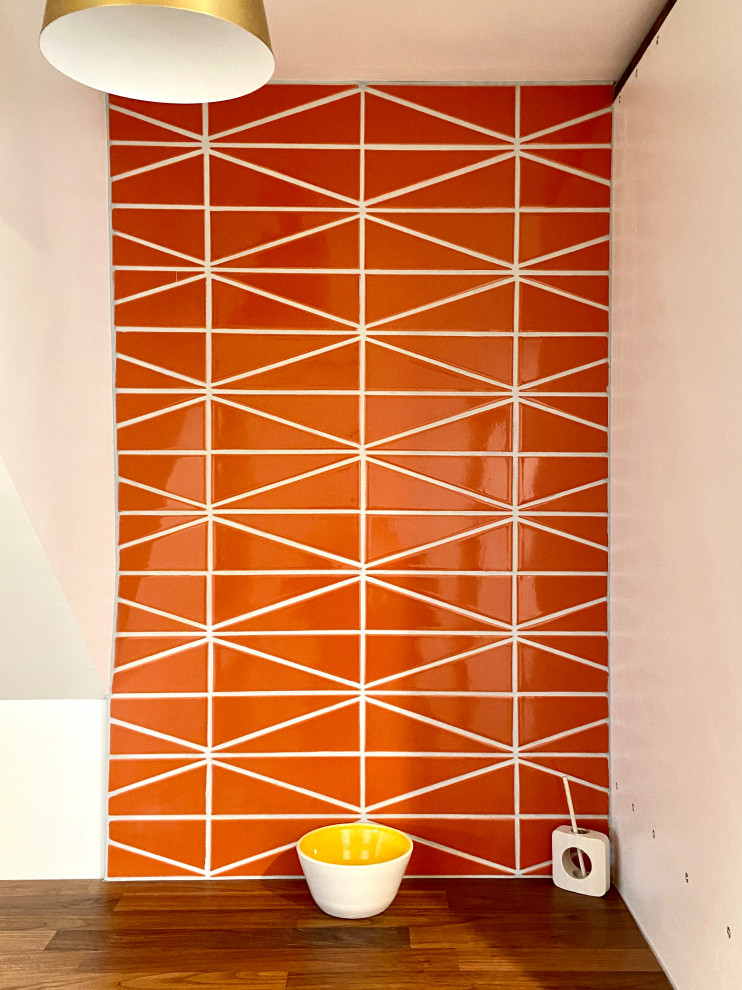 Bild på en mellanstor retro tvättstuga, med orange stänkskydd, stänkskydd i keramik och orange väggar