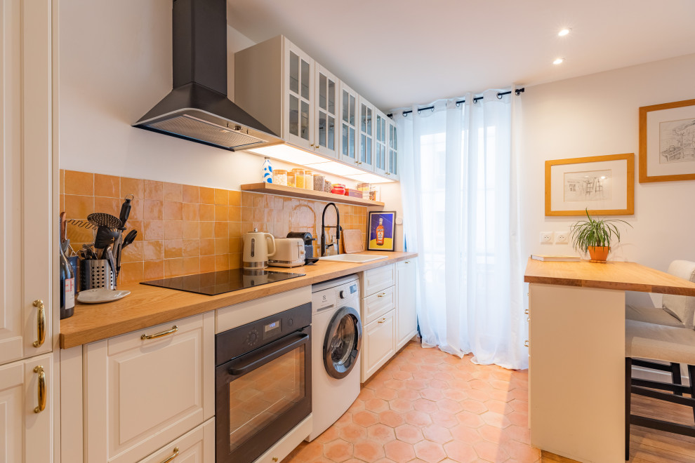 Photo of a mid-sized modern galley open plan kitchen in Paris with an undermount sink, beaded inset cabinets, white cabinets, laminate benchtops, orange splashback, ceramic splashback, panelled appliances, terra-cotta floors, with island, orange floor and brown benchtop.