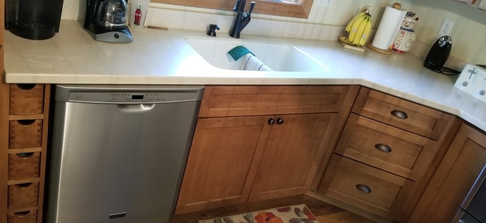 Example of a transitional l-shaped eat-in kitchen design with a double-bowl sink, shaker cabinets, solid surface countertops, stainless steel appliances and an island
