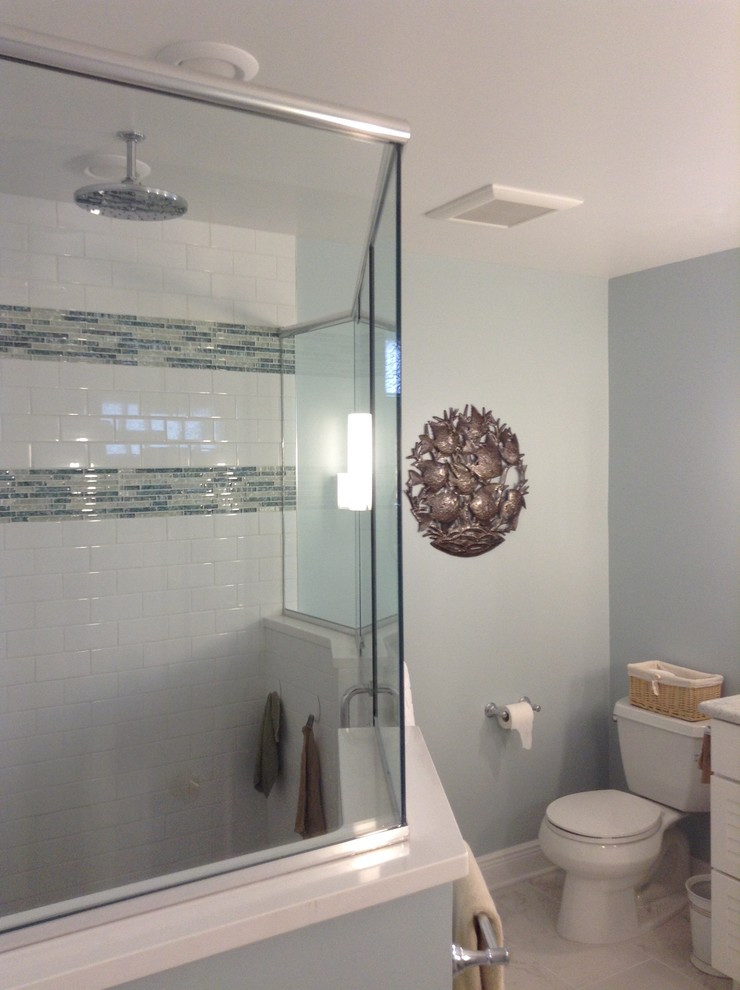 This is an example of a large beach style master bathroom in New York with louvered cabinets, white cabinets, a corner shower, a two-piece toilet, multi-coloured tile, blue walls, porcelain floors, quartzite benchtops and an undermount sink.