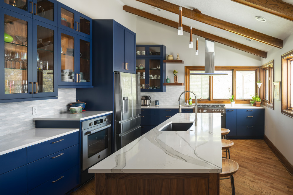 Photo of a mid-sized midcentury l-shaped open plan kitchen in Kansas City with an undermount sink, glass-front cabinets, blue cabinets, quartz benchtops, multi-coloured splashback, black appliances, medium hardwood floors, with island, white benchtop and vaulted.