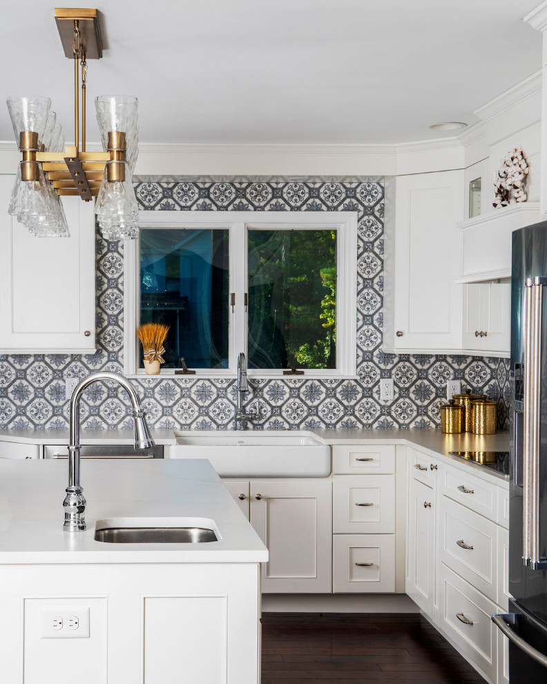 Inspiration for a mid-sized transitional l-shaped eat-in kitchen in St Louis with a farmhouse sink, recessed-panel cabinets, white cabinets, quartz benchtops, blue splashback, ceramic splashback, stainless steel appliances, medium hardwood floors, with island, brown floor and white benchtop.