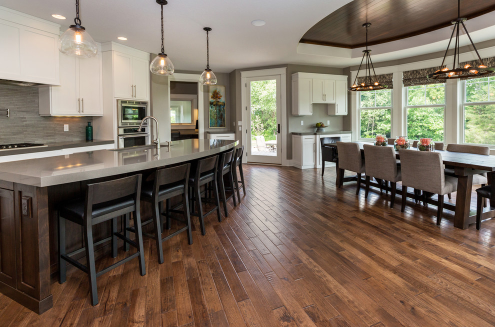 Inspiration for a large transitional l-shaped dark wood floor eat-in kitchen remodel with an undermount sink, shaker cabinets, white cabinets, solid surface countertops, gray backsplash, stainless steel appliances and an island
