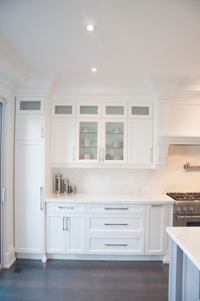Inspiration for a large transitional l-shaped dark wood floor and brown floor enclosed kitchen remodel in Toronto with an undermount sink, shaker cabinets, white cabinets, quartz countertops, white backsplash, marble backsplash, stainless steel appliances, an island and white countertops