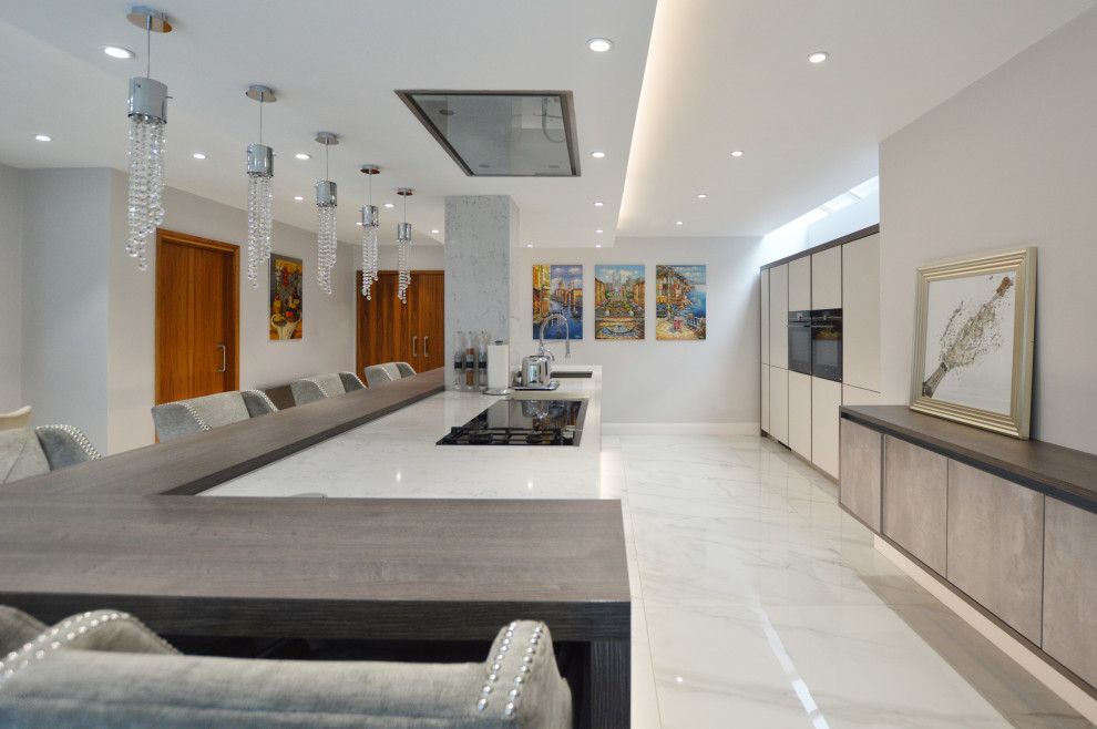 Photo of an expansive modern single-wall eat-in kitchen in Buckinghamshire with a drop-in sink, flat-panel cabinets, quartzite benchtops, stainless steel appliances, with island and white benchtop.