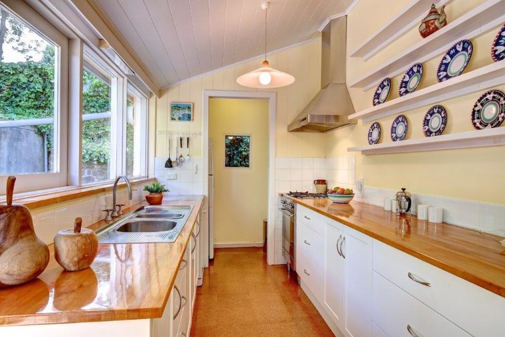 Mid-sized country galley eat-in kitchen in Adelaide with a double-bowl sink, recessed-panel cabinets, white cabinets, wood benchtops, white splashback, ceramic splashback, stainless steel appliances, cork floors, beige floor and beige benchtop.