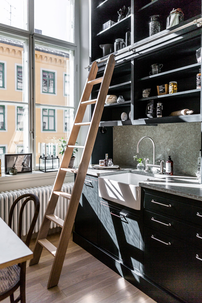 Design ideas for a mid-sized scandinavian single-wall kitchen in Stockholm with a farmhouse sink, flat-panel cabinets, black cabinets, grey splashback, stone slab splashback, dark hardwood floors and no island.