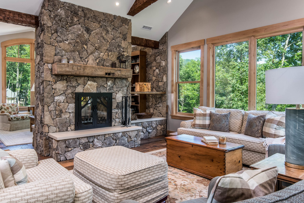 This is an example of a mid-sized country enclosed living room in Other with grey walls, medium hardwood floors, a two-sided fireplace, a stone fireplace surround, brown floor and no tv.