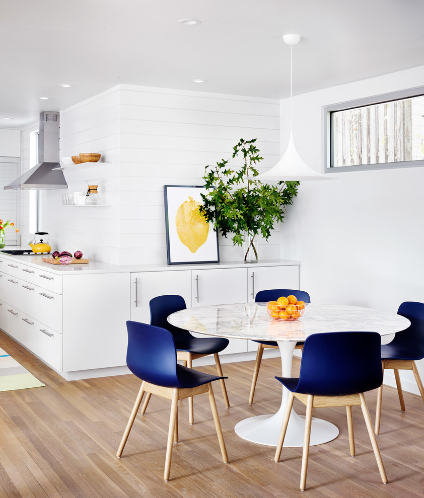 This is an example of a contemporary kitchen/dining combo in Austin with white walls and light hardwood floors.
