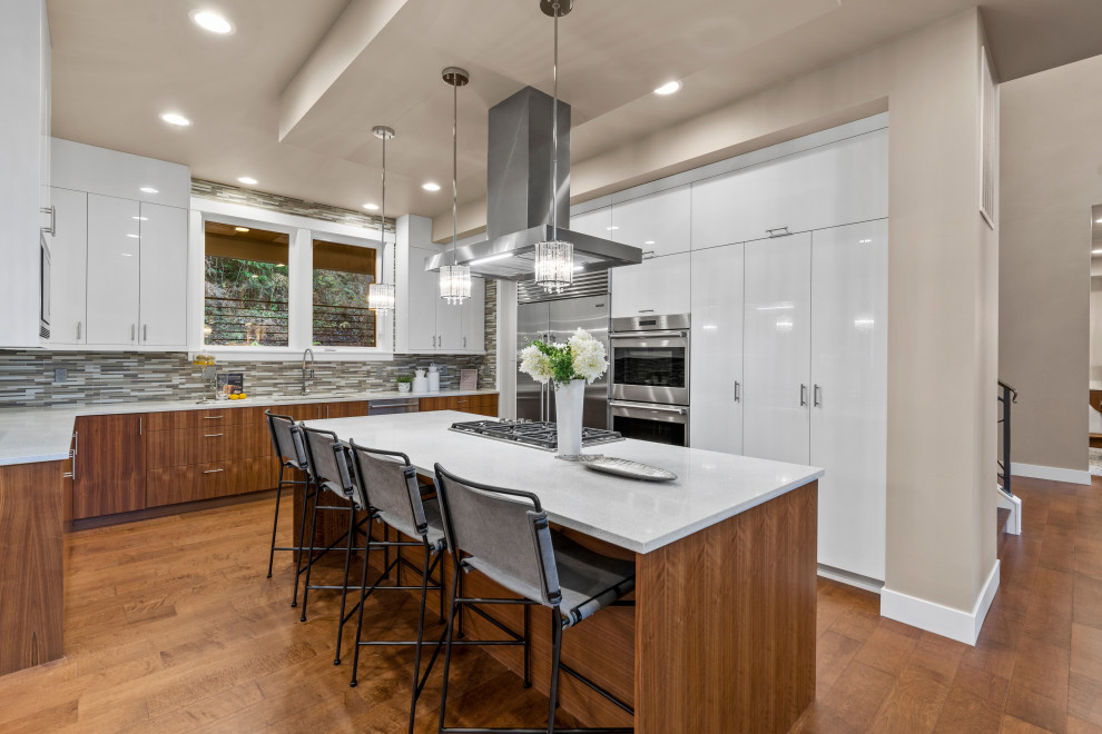 Example of a trendy u-shaped medium tone wood floor and brown floor open concept kitchen design in Seattle with an undermount sink, flat-panel cabinets, white cabinets, quartz countertops, multicolored backsplash, matchstick tile backsplash, stainless steel appliances, an island and white countertops