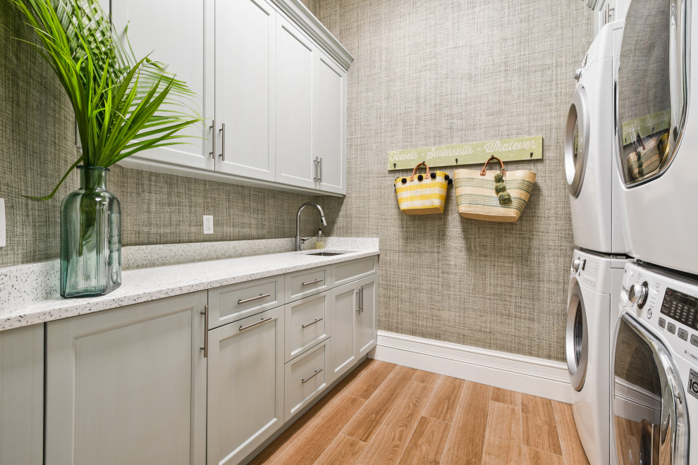Design ideas for a large tropical u-shaped laundry room in Other with an undermount sink, beaded inset cabinets, white cabinets, quartzite benchtops, blue splashback, glass tile splashback, light hardwood floors, brown floor, beige benchtop and wood.