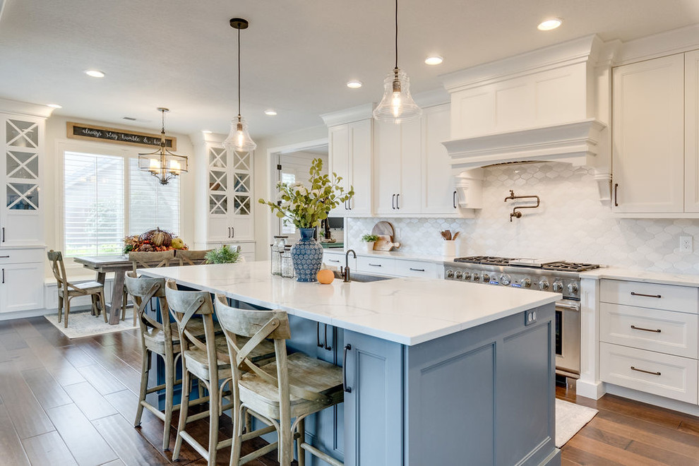 Photo of a beach style eat-in kitchen in Salt Lake City with shaker cabinets, white cabinets, white splashback, stainless steel appliances, medium hardwood floors, with island and white benchtop.