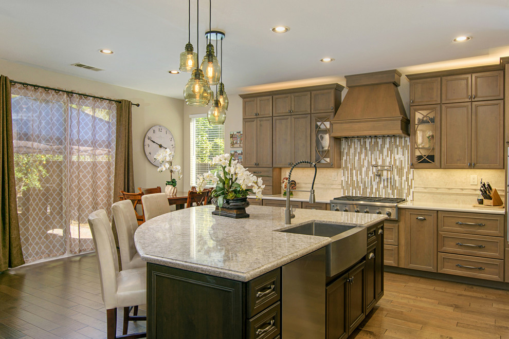 Open concept kitchen - large transitional l-shaped medium tone wood floor and brown floor open concept kitchen idea in San Diego with a farmhouse sink, recessed-panel cabinets, medium tone wood cabinets, paneled appliances, an island, quartz countertops, beige backsplash and travertine backsplash