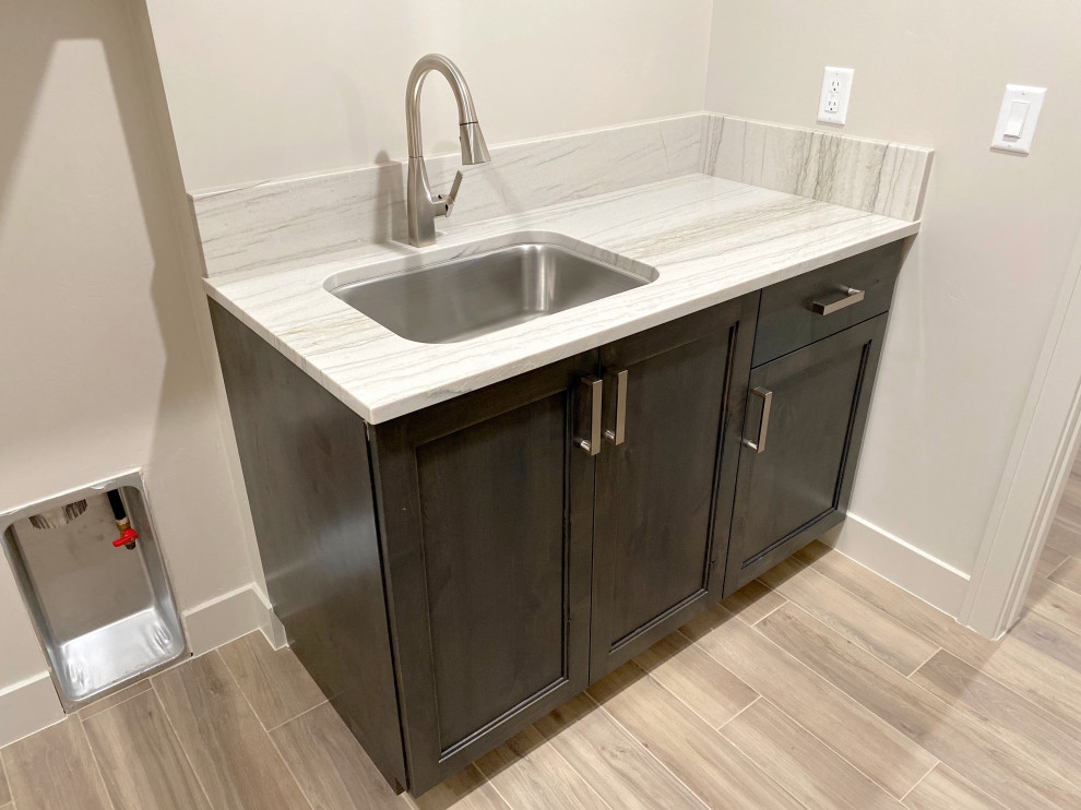 Inspiration for a modern galley ceramic tile and brown floor utility room remodel in Salt Lake City with an utility sink, raised-panel cabinets, brown cabinets, quartzite countertops, white backsplash, white walls, a side-by-side washer/dryer and white countertops