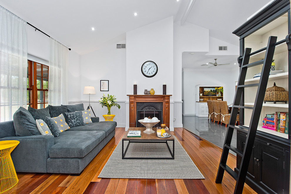Photo of a transitional open concept living room in Brisbane with white walls, medium hardwood floors, a standard fireplace and a wood fireplace surround.