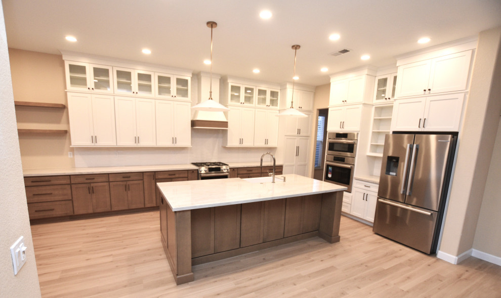 Example of a large transitional l-shaped vinyl floor and beige floor open concept kitchen design with a farmhouse sink, shaker cabinets, light wood cabinets, quartz countertops, white backsplash, ceramic backsplash, stainless steel appliances, an island and white countertops