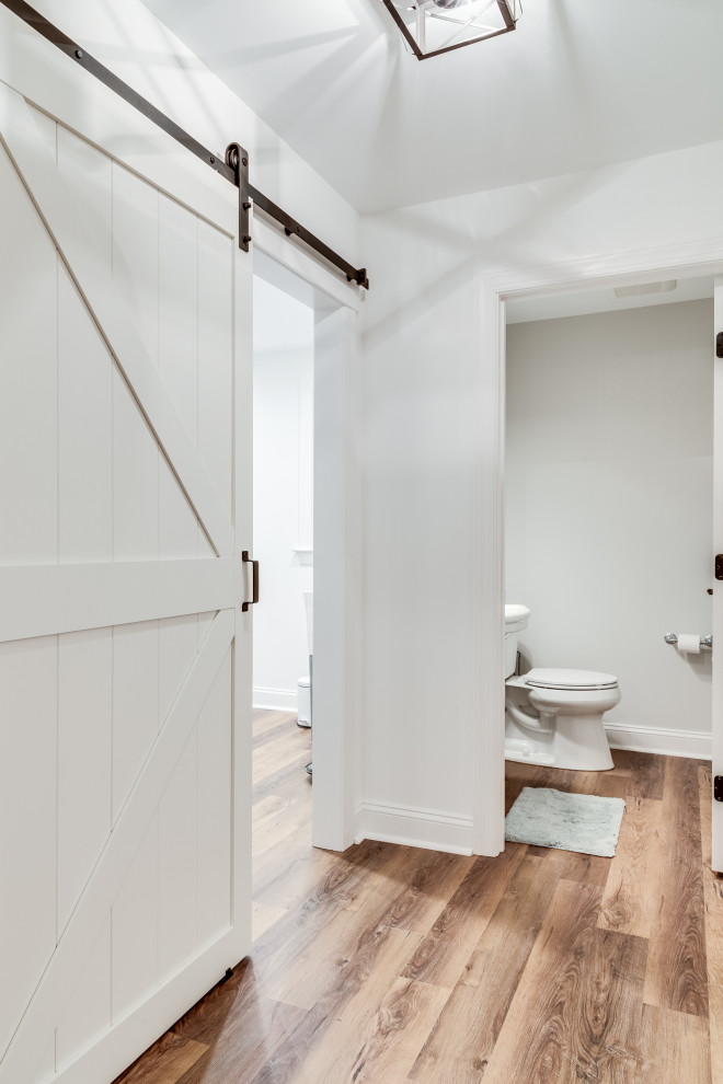 Photo of a mid-sized country single-wall utility room in Baltimore with an utility sink, shaker cabinets, white cabinets, grey walls, laminate floors and brown floor.