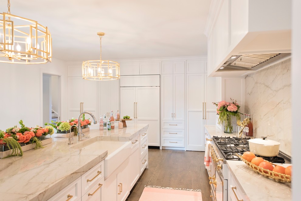 Example of a large transitional l-shaped medium tone wood floor and brown floor open concept kitchen design with a farmhouse sink, recessed-panel cabinets, white cabinets, quartzite countertops, white backsplash, stone slab backsplash, paneled appliances and an island